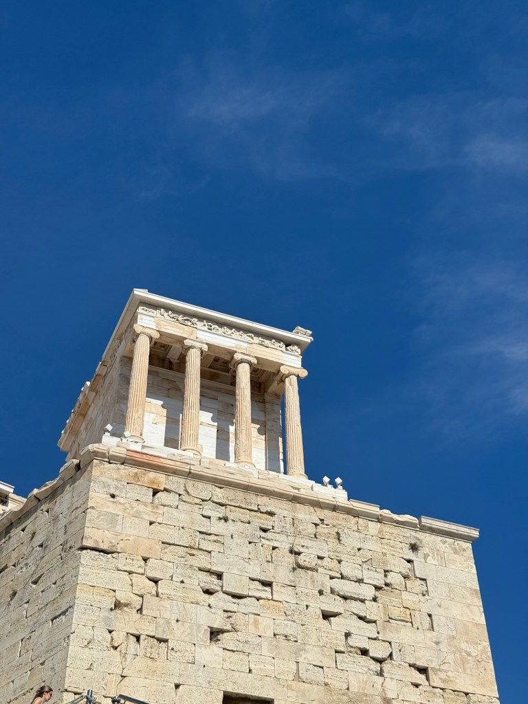 Close-up view of a classical Greek temple on a stone structure against a clear blue sky.