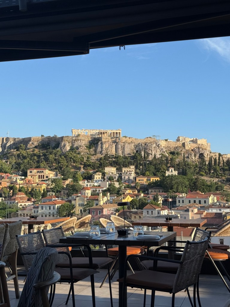 View from a restaurant terrace overlooking colorful houses and the Acropolis in Athens under a clear blue sky.