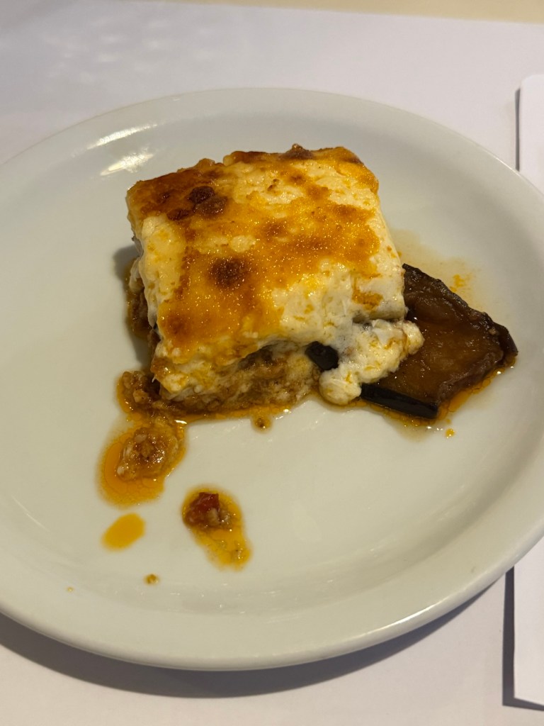 A serving of baked dish with a golden crust, layered with soft cheese and garnished with a sweet sauce on a white plate.